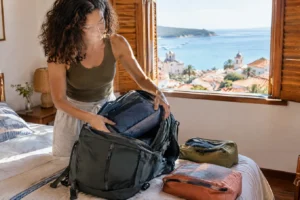 Viajante guardando cubos organizadores dentro da mochila aberta sobre a cama de uma pousada