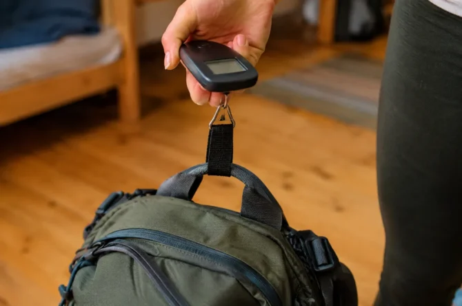 Close de mão segurando balança de bagagem presa à alça superior de uma mochila cargueira