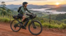 Cicloturista com bicicleta elétrica carregada de bolsas em estrada de terra entre montanhas ao amanhecer