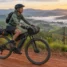 Cicloturista com bicicleta elétrica carregada de bolsas em estrada de terra entre montanhas ao amanhecer
