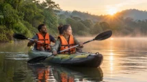 Dupla remando caiaque inflável em lagoa calma cercada de mata ao amanhecer, ambos com colete salva-vidas