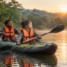 Dupla remando caiaque inflável em lagoa calma cercada de mata ao amanhecer, ambos com colete salva-vidas