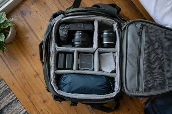 Câmera mirrorless, lente extra, baterias e cartões organizados em divisória acolchoada de mochila