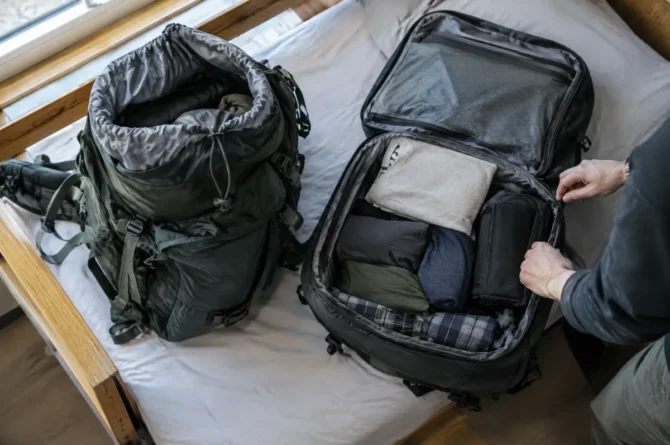 Duas mochilas abertas lado a lado sobre a cama de um hostel, uma de abertura superior e outra com abertura tipo mala