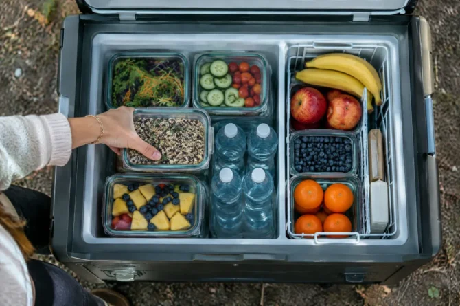 Interior de geladeira portátil organizado com potes de alimentos, garrafas de água e divisória
