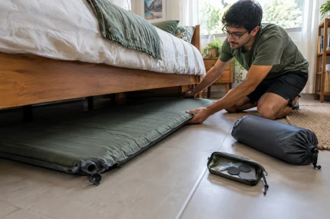Isolante autoinflável aberto com a válvula aberta embaixo de uma cama, ao lado de kit de reparo