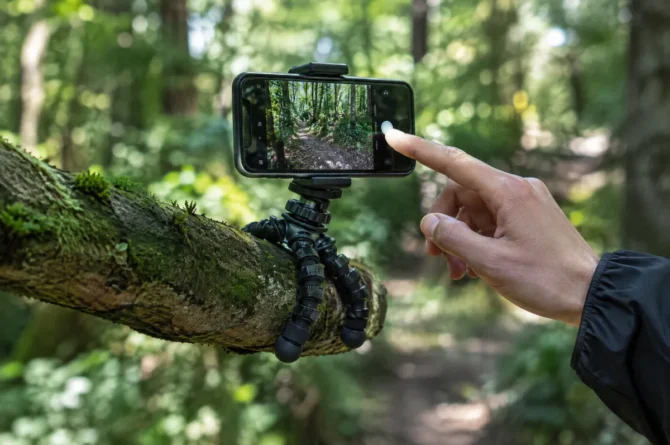 Mini tripé de pernas flexíveis enrolado num galho segurando um celular na trilha