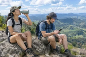 Dupla de trilheiros com mochilas de ataque fazendo pausa em mirante de serra