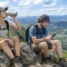 Dupla de trilheiros com mochilas de ataque fazendo pausa em mirante de serra