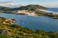 Vista do alto de uma lagoa com barcos, dunas e praia oceânica, em paisagem de ilha no sul do Brasil