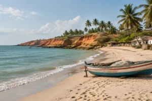 Praia tranquila de vilarejo com falésias avermelhadas, coqueiros e barco de pesca na areia