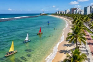 Orla urbana de mar verde-esmeralda com jangadas coloridas, coqueiros e calçadão no Nordeste