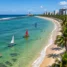 Orla urbana de mar verde-esmeralda com jangadas coloridas, coqueiros e calçadão no Nordeste