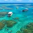 Piscinas naturais azul-turquesa sobre recifes de coral em alto-mar, com barcos e pessoas flutuando