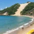 Praia urbana em curva terminando em grande duna com vegetação, com guarda-sóis na areia