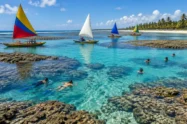 Piscinas naturais de águas azul-turquesa entre arrecifes, com jangadas coloridas e coqueiros