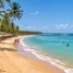 Praia de areia dourada com coqueiros, barracas coloridas e mar azul-turquesa no sul da Bahia