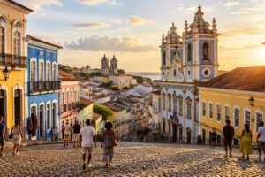 Largo de pedra em ladeira com casarões coloniais coloridos e torres de igreja ao entardecer