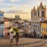 Largo de pedra em ladeira com casarões coloniais coloridos e torres de igreja ao entardecer