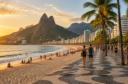 Orla de praia com calçadão de pedras portuguesas, coqueiros e montanhas ao fundo no Rio de Janeiro