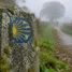 Marco de pedra com a vieira do Caminho de Santiago em trilha rural da Galícia com névoa