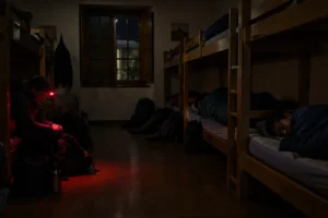 Peregrino arrumando a mochila em silêncio com lanterna vermelha, regra de convivência nos albergues do Caminho de Santiago