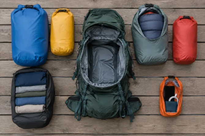 Sacos estanques de cores diferentes organizando roupa, saco de dormir e eletrônicos ao lado da mochila