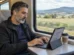 Viajante usando um tablet com capa teclado na mesa de um trem com paisagem rural passando pela janela